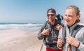 Father with teenager son with backpacks walking by the sandy seaside beach. They smiling and looking at the camera. Active happy