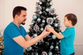 Father and toddler son decorating Christmas tree together, dad giving to child big silver ball. Family winter holidays preparation Royalty Free Stock Photo