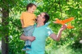 Father and son playing together with orange airplane outdoors: boy is sitting on shoulder of man, both dad and kid are smiling Royalty Free Stock Photo