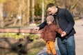 Father and toddler son stand in a park near the city lake on a sunny spring day.