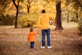 Father and toddler son walking holding hands in autumn park, view from behind. Dad and child going to play football outdoors Royalty Free Stock Photo