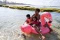 Father and two daughters ride flamingo buoy on the beach Royalty Free Stock Photo