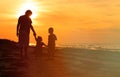 Father and two kids walking on beach at sunset