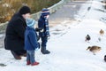 Father and two little siblings boys feeding ducks in winter. Royalty Free Stock Photo