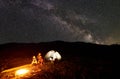 Father and two sons hikers having a rest at camping in mountains under night sky full of stars and Milky way