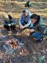 A father and two sons are sitting by the fire and roasting sausages on skewers Royalty Free Stock Photo