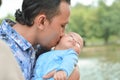 Asian father kisses baby on his arm with love near lake at outdoor park in day time Royalty Free Stock Photo