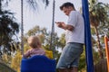 Father with child on a playground looking on phone ignoring his baby swinging. Royalty Free Stock Photo