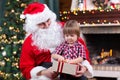 Father weared Santa Claus and kid boy open gift sitting near by Christmas tree at fireplace Royalty Free Stock Photo