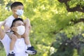 Father wearing face mask while playing a piggyback ride with his son in the park