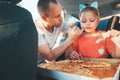 Father wiping gently daughter\'s mouth while eating just cooked Italian pizza during family car trip brake stop. Happy family