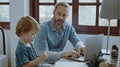 Father working from home office using laptop sit at table with cute little son playing nearly to disturb Royalty Free Stock Photo