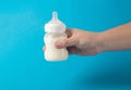Father& x27;s hand with a baby bottle with milk formula on a blue background shakes the mixture to mix. Nutrition of