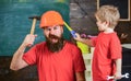 Fatherhood concept. Father, parent with beard in protective helmet teaching little son to use different tools in school