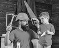 Fatherhood concept. Father, parent with beard in protective helmet teaching son to use different tools in school