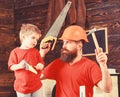 Fatherhood concept. Father, parent with beard in protective helmet teaching son to use different tools in school