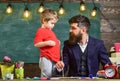 Fatherhood concept. Teacher with beard, father teaches little son to draw in classroom, chalkboard on background