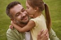 Fathers day. Cute little girl hugging and kissing her happy dad while sitting on a green grass Royalty Free Stock Photo