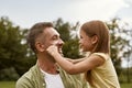 Fathers day. Cute little girl playing with her daddy while visiting park on a summer day, touching his cheeks and Royalty Free Stock Photo