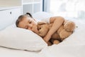 Fatigued cute girl hugging toy bear and coughing in bed