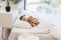 Fatigued cute girl hugging toy bear and coughing in bed