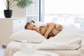 Fatigued cute girl hugging toy bear and coughing in bed