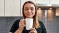 Favorite drink. Close up of young curvy woman closing her eyes and smiling while drinking tea or coffee in the kitchen Royalty Free Stock Photo