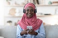 Favorite Leisure. Black muslim girl using smartphone and wireless headphones at home Royalty Free Stock Photo