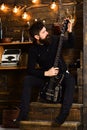 Favourite activity. Man bearded musician enjoy evening with bass guitar, wooden background. Man with beard holds black