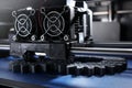 FDM 3D-printer manufacturing spur gears from silver-gray filament on blue print tape in bright light