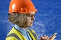 Feamle Engineer in the construction helmet with mobile phone on blue background, woman using smartphone app for warehouse Royalty Free Stock Photo