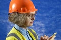 Feamle Engineer in the construction helmet with mobile phone on blue background, woman using smartphone app for warehouse