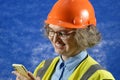 Feamle Engineer in the construction helmet with mobile phone on blue background, woman using smartphone app for warehouse