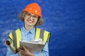 Feamle Engineer in the construction helmet and yellow vest with mobile phone and documents on blue background