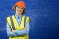 Feamle Engineer in the construction helmet and yellow vest with mobile phone and documents on blue background