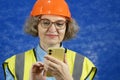 Feamle Engineer in the construction helmet and yellow vest with mobile phone and documents on blue background