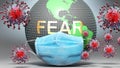 Fear and covid - Earth globe protected with a blue mask against attacking corona viruses to show the relation between Fear and
