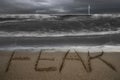 Fear word hand written on sand beach with stormy ocean