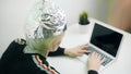 Fearful woman with aluminum hat working on laptop. Protection against 5g and mind reading and control