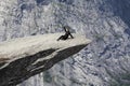 Fearless woman sitting on Trolltunga rock formation and waving hand. Jutting cliff is in Odda, Hordaland county, Norway