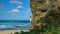 Fearless young woman attempts to climb a cliff on the rocky shore of Barbados.