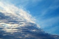 Feathery clouds in the blue sky are illuminated by the rays of the sun, setting over the horizon