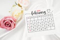 February 2024 calendar page and rose flower on white satin textile Royalty Free Stock Photo