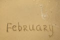 February - handwritten on the soft beach sand.
