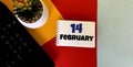 February 14 on a multicolored background on a white notebook.Next to it is an artificial flower in a pot .