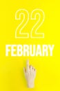 February 22nd. Day 22 of month, Calendar date.Hand finger pointing at a calendar date on yellow background.Winter month, day of