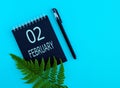 February 2th. Day 2 of month, Calendar date. Black notepad sheet, pen, fern twig, on a blue background