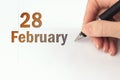 February 28th. Day 28 of month, Calendar date. The hand holds a black pen and writes the calendar date. Winter month, day of the