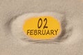 February 2. 2th day of the month, calendar date. Hole in sand. Yellow background is visible through hole