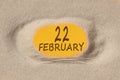 February 22. 22th day of the month, calendar date. Hole in sand. Yellow background is visible through hole